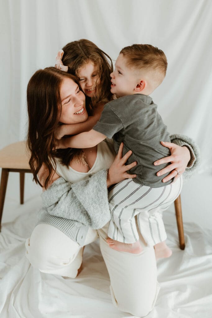 Mother laughing as her two children jump on her during indoor motherhood mini session in Southern Ohio